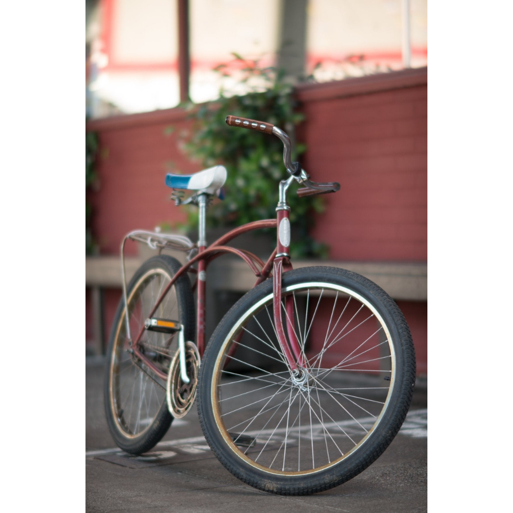 Old-fashioned steel Schwinn bicycle with a blue glitter saddle and curved red glitter top tube with a curvy handlebar that has dark brown leather grips sew-on. 