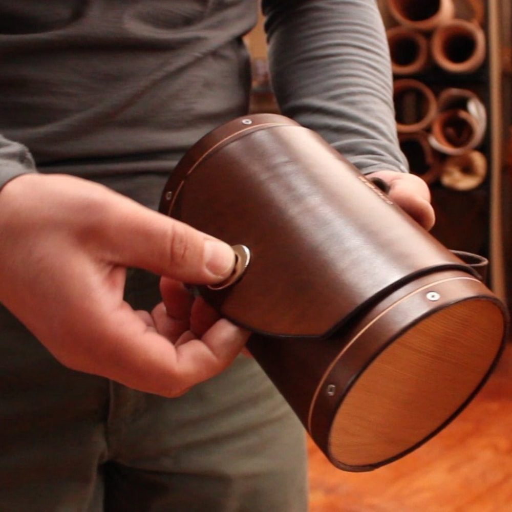 Hands holding dark brown leather barrel bag off bicycle bag. The hand is slightly larger than the bag and can hold it comfortably.