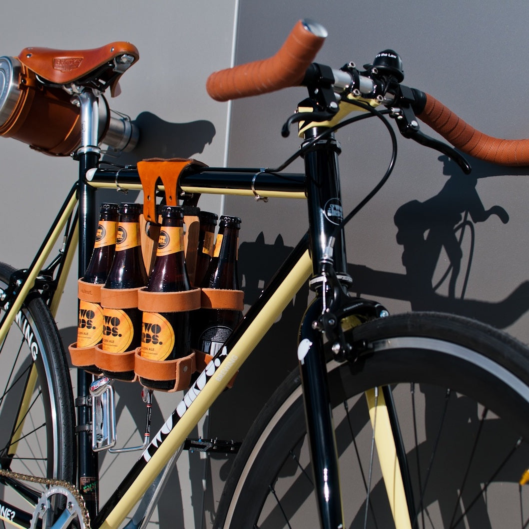 Honey leather and bamboo six-pack held on the top tube of a black bicycle with a 6-pack beer carrier, the 6-pack frame cinch on a custom branded bike for an Australian brewery