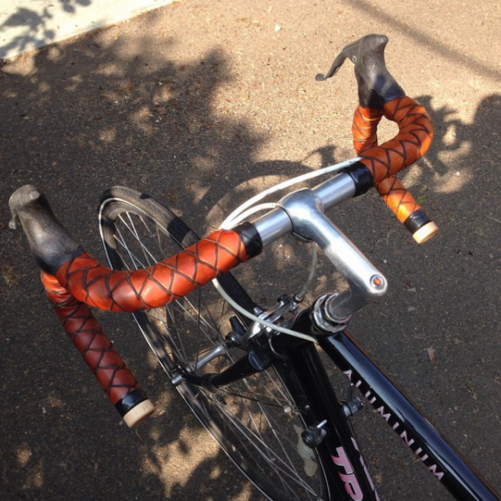 Black bike with honey braided leather bar tape on a sunny day.