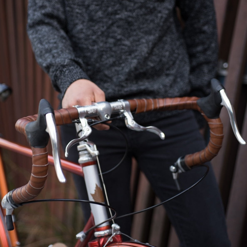 Angle view looking down an orange steel framed bicycle from the handlebars, which are wrapped in dark brown leather bar tape.