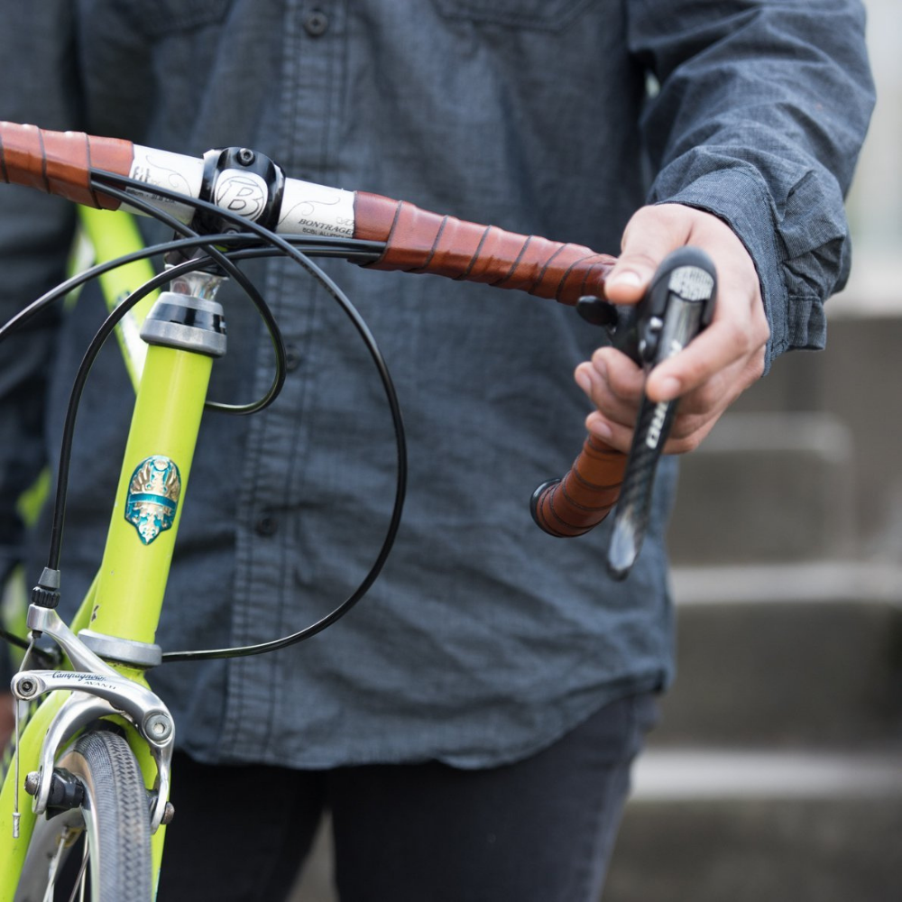 Front-on view of a lime green bicycle being carried by an African-American woman in a rain jacket using a Bicycle Frame Handle and the handlebars, which are wrapped in Dark Brown leather bar tape (close up)