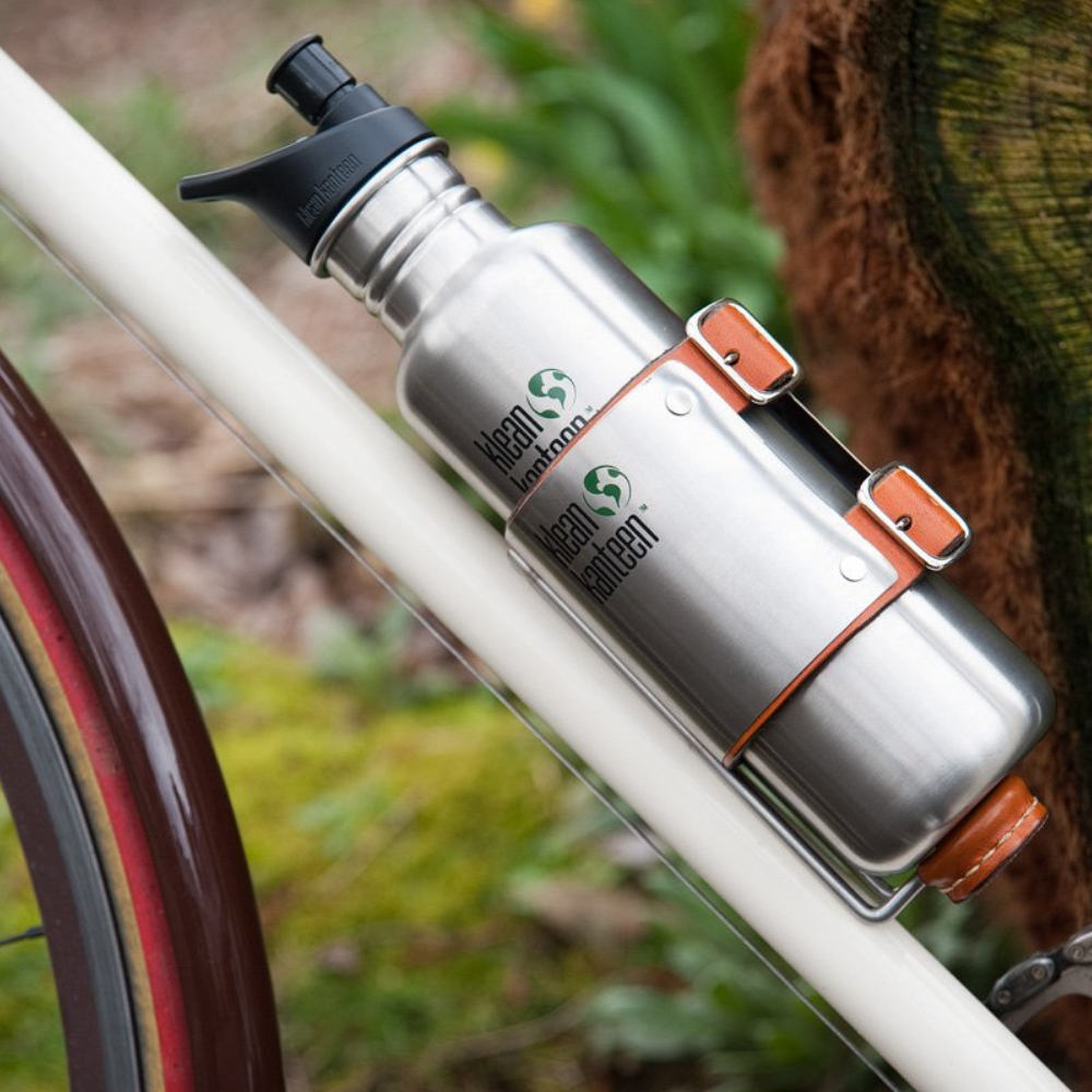 klean kanteen branded water bottle resting in the upcycle cage drink holder attached to a white bicycle frame