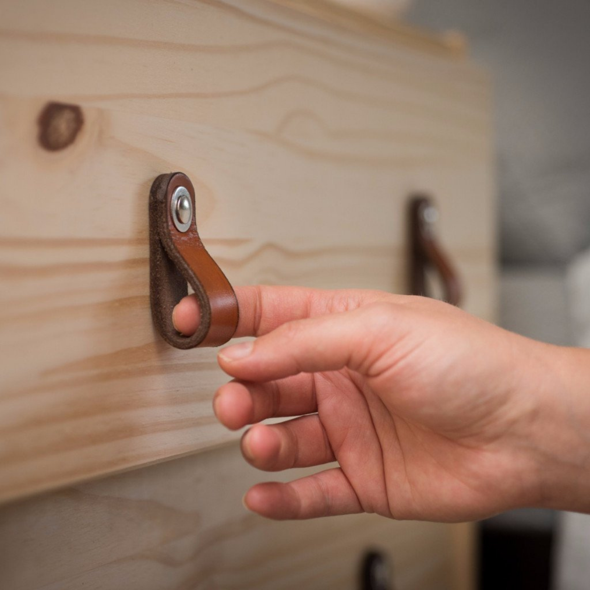 Woman's hand reaching out to a small honey-colored leather handle and pulling out a knotty pine wood drawer