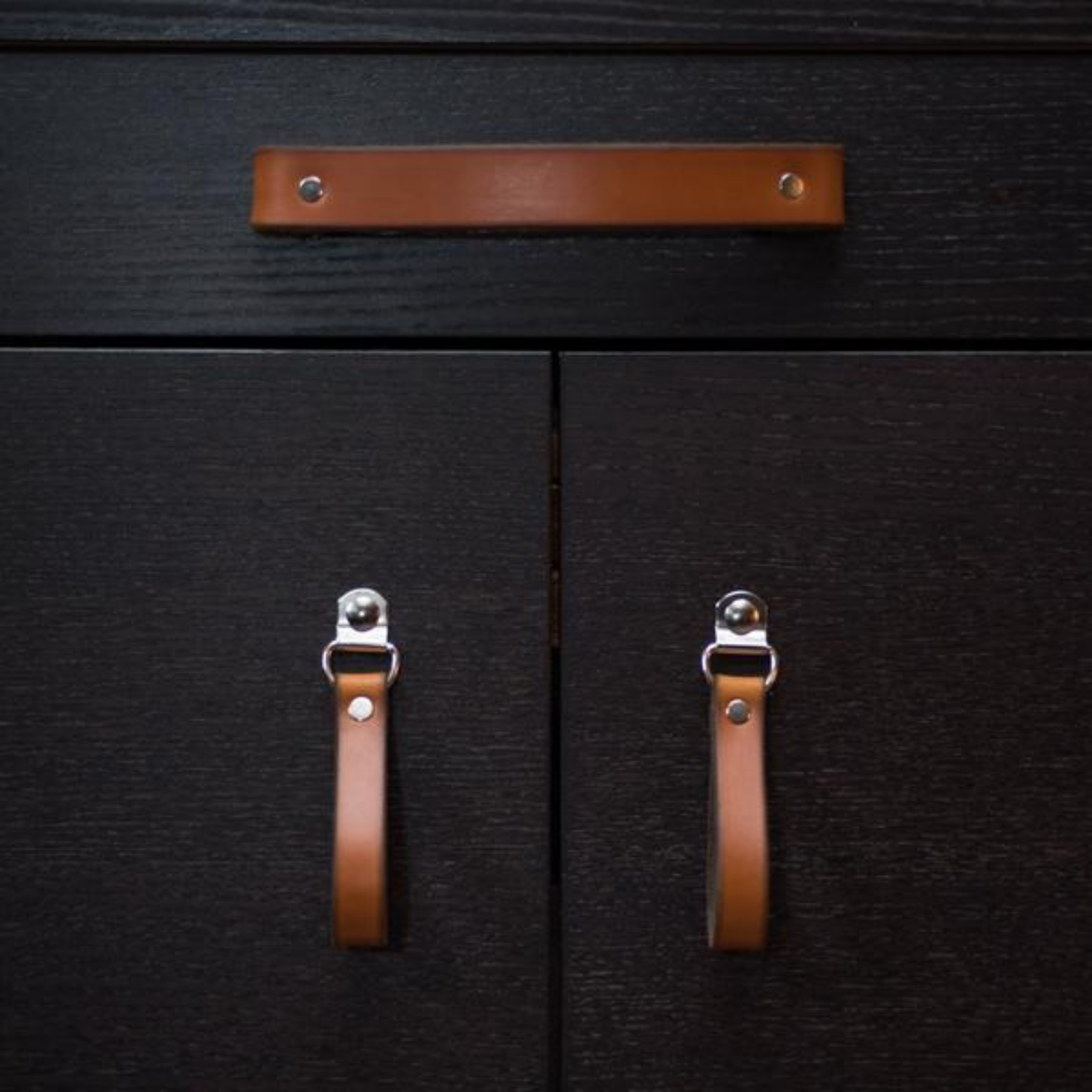 Still life scene of an IKEA TV buffet sideboard cabinet in black-brown finish with Walnut Studiolo honey leather hinged Burnside knobs and the Tilikum leather handle. 