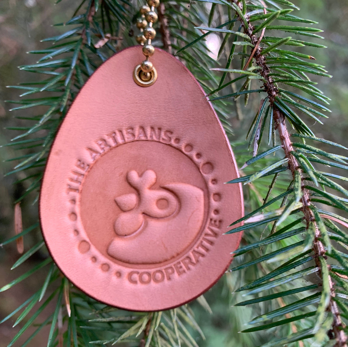 Leather fundraiser for Artisans Cooperative hung from a tree like a Christmas ornament